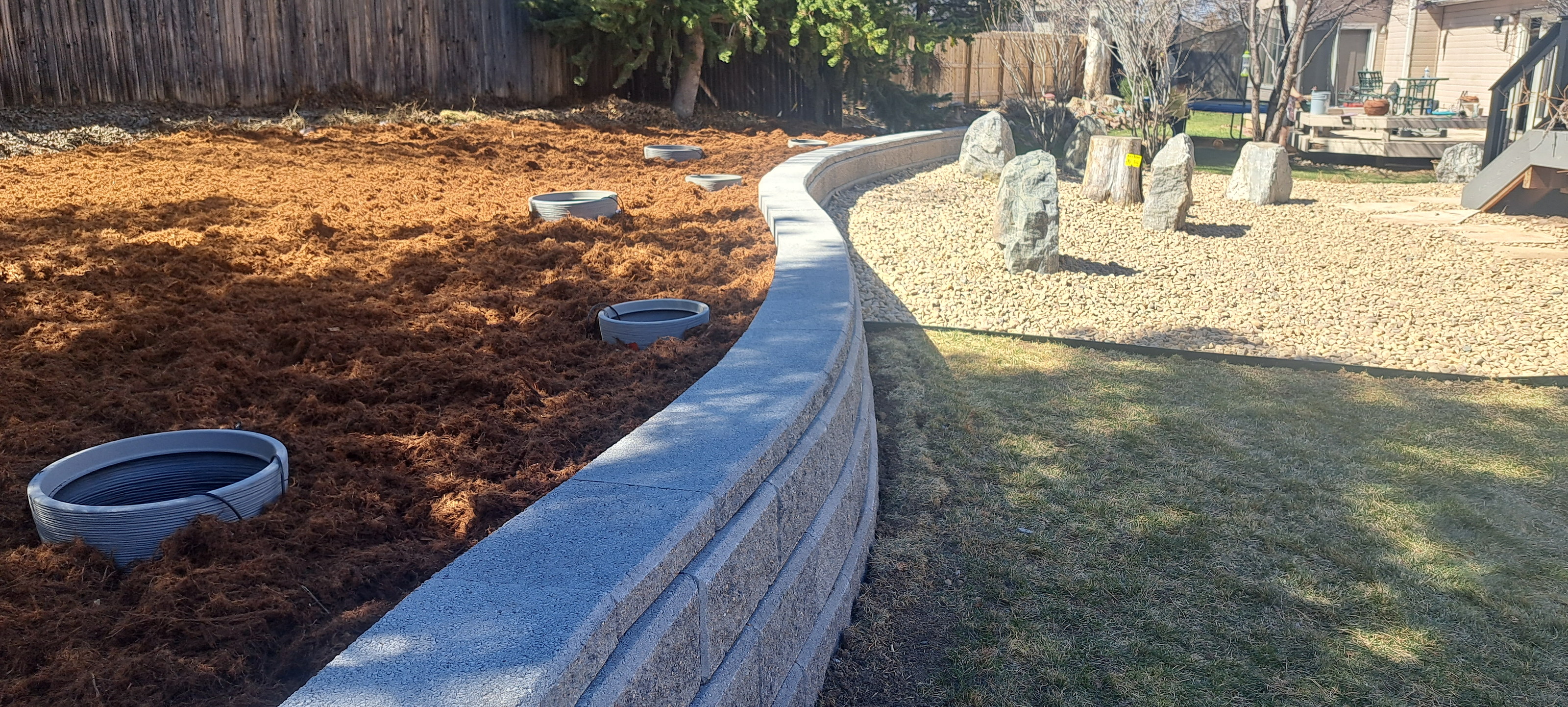 Long curved segmental block retaining wall with capstones, mulch, and boulders.
