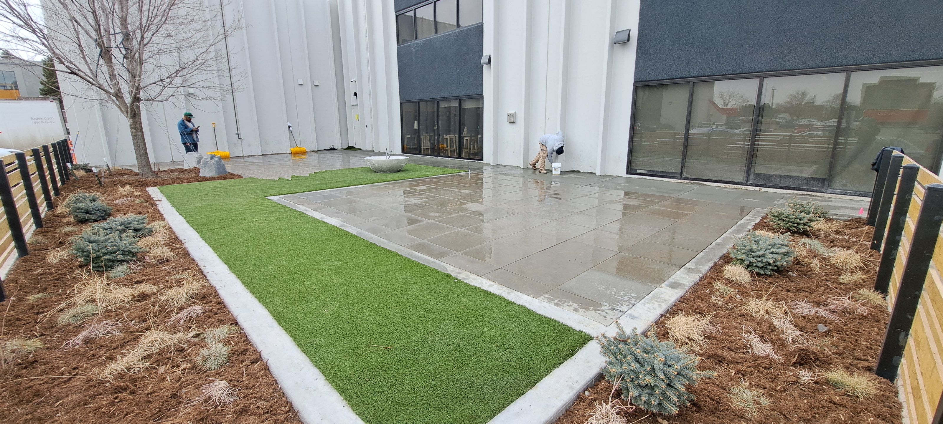 New green turf strips beside a concrete pad in front of a white building with dark windows.