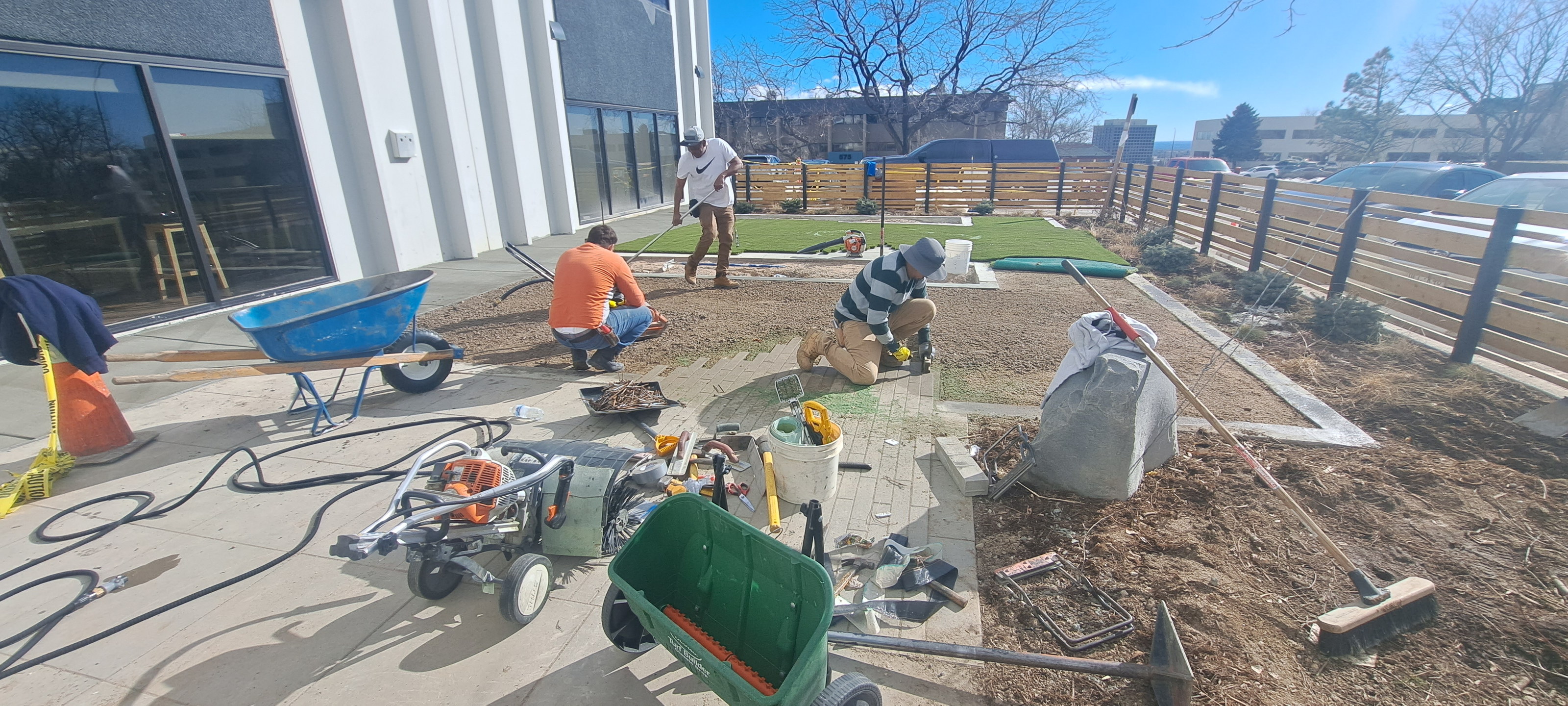 Workers and wheelbarrows during a turf installation beside a white commercial building.