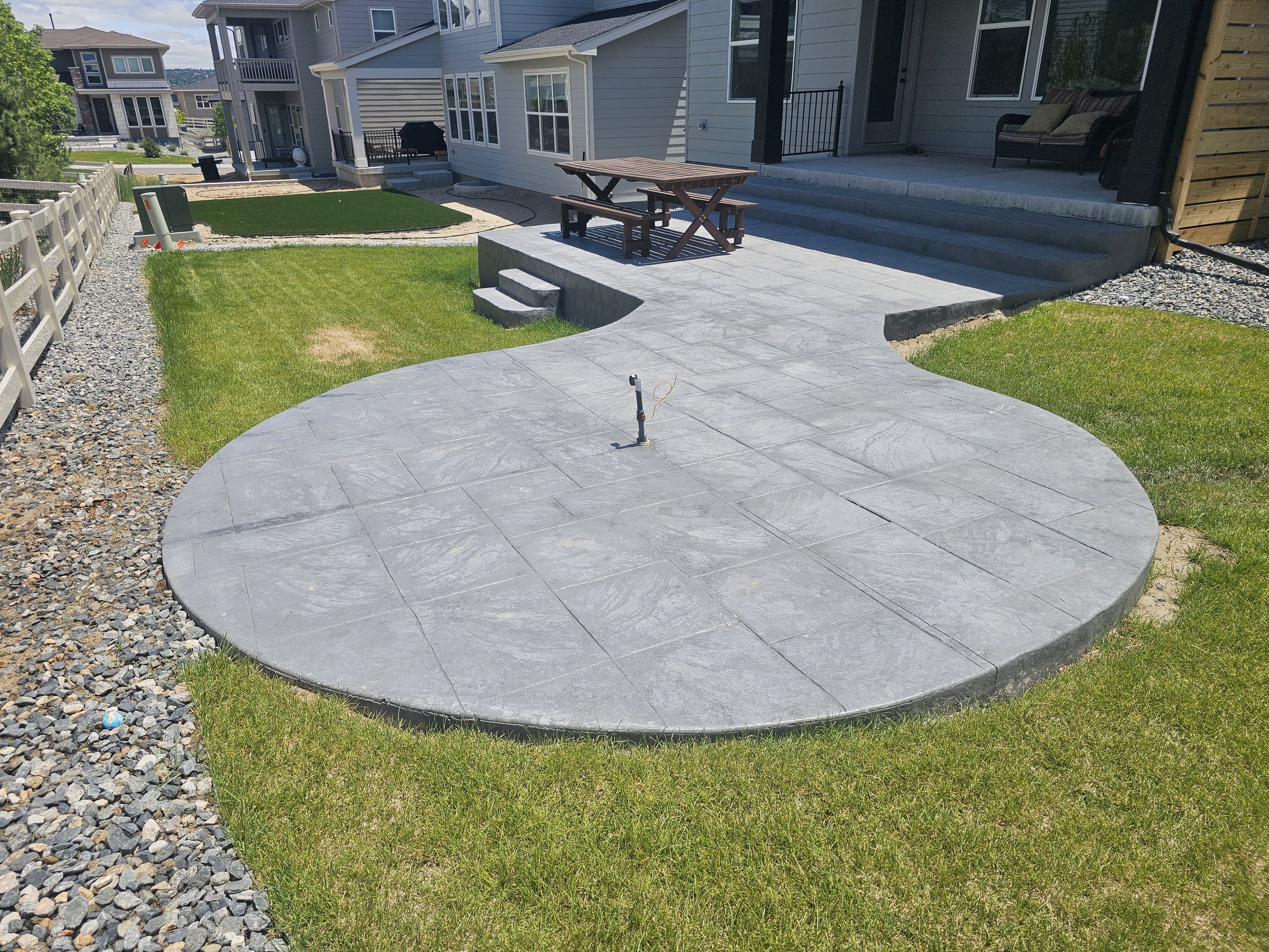 Round stamped concrete patio and steps in a backyard, with an unfinished fixture in the foreground.