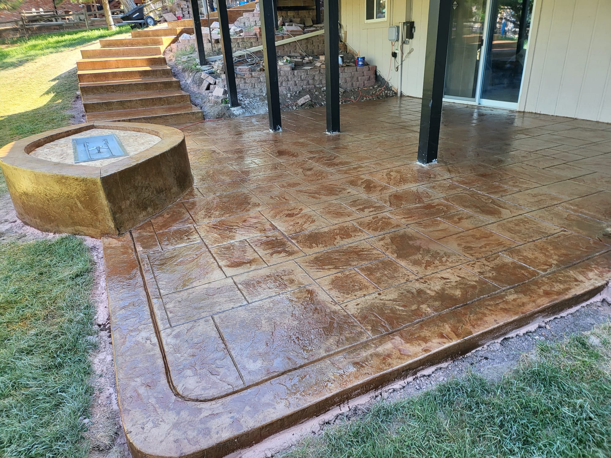 Glossy warm-brown decorative concrete beside a house and a round stone planter.