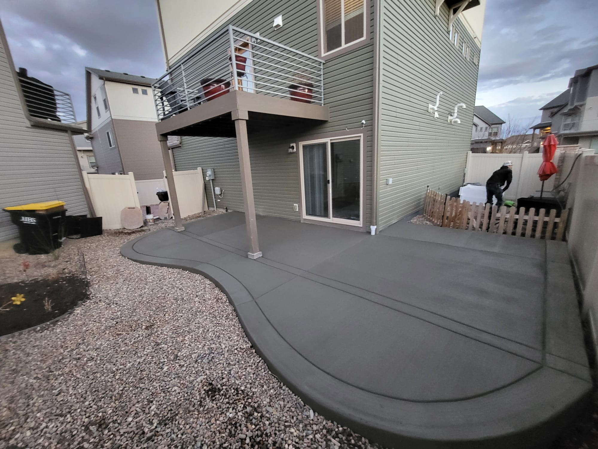 Smooth gray concrete patio curving around the back of a two-story house.